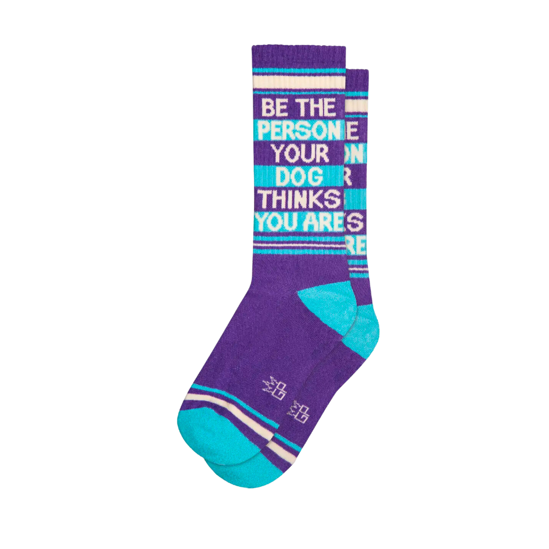 Purple socks with teal and white stripes with white text "Be The Person Your Dog Thinks You Are". Live by your mantra: step out and be proud of yourself — your pup already is! Stride confidently and always be your best, wherever you are — crafted in the United States from 61% cotton, 36% nylon, and 3% spandex.