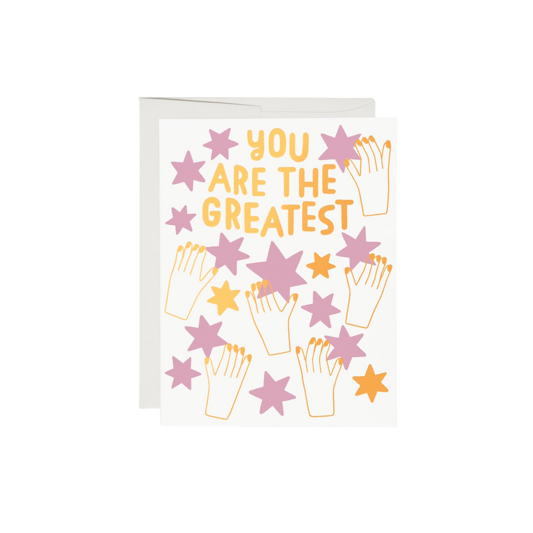 This 5.5"x4.25" card has a stars and says you are the greatest. gold illustration of hands  holding pink and gold stars.  100lb heavyweight card stock, foil-stamped offset printing, and a design illustrated by Anke Weckmann. Additionally, this card is blank inside and printed in the USA on recycled paper.  